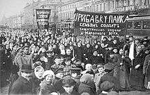 A large gathering of people outside, some holding banners