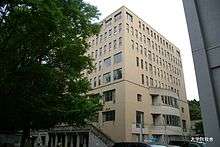 Square, tan building, with large tree next to it