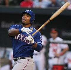 A man in a blue baseball helmet and a blue baseball jersey swinging a blond wooden bat