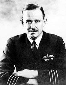 Half-length portrait of moustachioed man in military uniform, with aviator's wings on left breast pocket and four stripes on jacket forearms