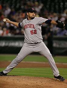 A man wearing a gray pinstriped baseball uniform and navy-blue cap throwing a baseball with his right hand