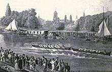 A river scene, with two eight-oared boats racing in the middle of the river, one just in front of the other. There are crowds on each bank and some sailing boats and barges by the far bank. In the distance, trees and church spires.