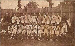 row of 11 men in striped kit sitting in front of another row of 11 men standing and dressed in plain kit, flanked by 4 other men