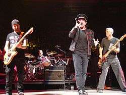 A color photograph of members of the band U2 performing on stage