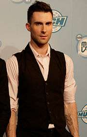 A man with a black vest and a white shirt posing on red carpet at an award show