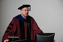 Middle-aged, bespectacled man in academic dress making a presentation