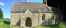 A very small stone church seen from the south with a prominent doorway, and a smaller chancel towards the right