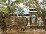 A picture of a fortified wall and gate between two trees.