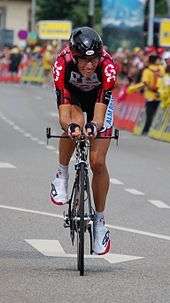 A cyclist on his bicycle, wearing a red and black jersey with white trim.