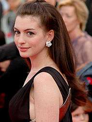 A woman with brown hair, wearing a dress, slightly looking over her shoulder while smiling.