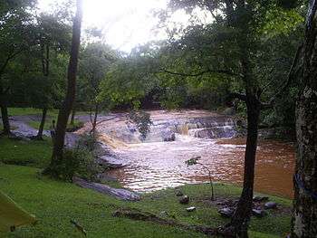 Wide stream with small waterfall, seen through trees from a campsite