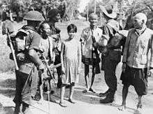 Soldiers carrying packs talk to civilians on a jungle road