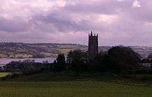 Church tower surrounded by trees with water in the background.