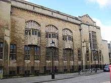 A cream coloured stone building with three projecting bay windows on the upper floor above which are sculptural groups