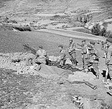 Gun in pit surrounded by crew on a hillside