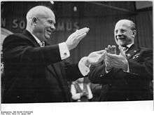 Two smiling men raise bouquets of flowers over their heads.