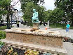 A large, rectangular, pink granite base with a smaller, aged bronze state of a boy and turtle sitting in the center of the base.