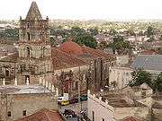 There is a large stone building in the center with a tall tower. Behind are several smaller buildings with red roofs.