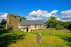 A small, low, simple church seen from the southwest with an elongated west tower surmounted by a saddleback roof