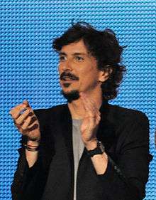 A man standing in front of a blue background, applauding