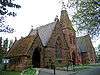 Two joined gabled sandstone chapels with a tower between in Gothic Revival style; the tower is truncated and has the metal skeleton of a spire on its top, the whole acting as a chimney