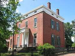 A brick house with a pillared entrance highlighted by the sun