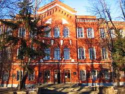 Brown, three-story building with arched windows and trees in front