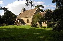 A small simple church seen from the southeast, with a south porch and a bellcote with a pyramidal roof at the west