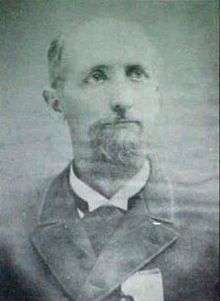 Head of a balding white man with a goatee, wearing a suit coat and tie.