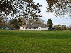 White building with grey roof in the middle of green grass area.