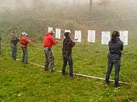 A line of people in front of targets drawing guns from holsters.