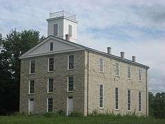 Three story gray rectangular building on a grassy hill