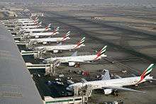 View of airport tarmac with terminal building and multiple airliners parked adjacent to it.