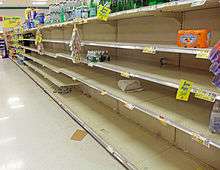 A supermarket aisle with a large section empy save for scattered packages of bottled water