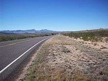 Image of FM 3078 passing through desert shrub land with the Davis Mountains looming in the distance.