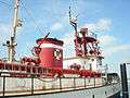 Photograph of the fireboat Duwamish at dock as a museum ship. The picture clearly shows several items of firefighting equipment, including water cannons, ladders, floodlights, pipelines, hose fittings, and the Seattle Fire Department seal on the funnel.