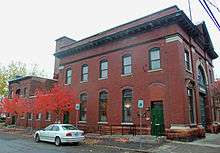 A two-story brick building with green trim seen from its side. There is a garage and a pediment in the front.