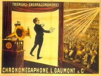 Illustration of a theater from the rear Right  of the stage. At the front of the stage a screen hangs down with the projected image of a tuxedoed man holding up a text and performing. In the foreground is a gramophone with two horns. In the background, a large audience is seated at orchestra level and on several balconies. The words "Chronomégaphone" and "Gaumont" appear at both the bottom of the illustration and, in reverse, at the top of the projection screen.