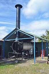 A silver coloured horizontal tube under a roof with a chimney projecting through it