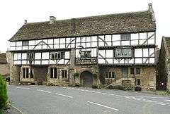 White fronted building with black beams prominent. Over the door is a sign saying The George Inn, Wadworths.