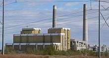 Multistory building with two large smokestacks; power lines in foreground