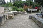 An outdoor patio made of sandy dirt with weathered, cut stones employed as seating and as borders for planters.