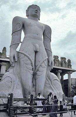 Giant grey stone statue of nude man with vines climbing legs to his arms