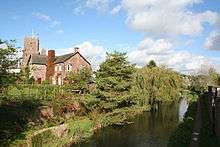 Inland water in front of trees, a house and a church