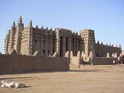 A large mud stone castle with hundreds of wooden poles sticking out around its upper half.