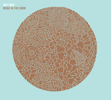 Pale blue album cover embossed with a brown circle made up from smaller parts. The words "Hot Chip" and, below it, "Made in the Dark" are displayed in the top left hand corner.