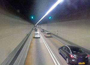 A two-lane road in a tunnel with plain brown sides and one overhead light strip.