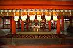 View through a hall (Haiden) with vermillion red beams and hanging lanterns to a space with standing lanterns beyond which there is another building with an altar.