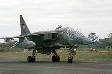 Jet aircraft in mostly green camouflage scheme taxiing.