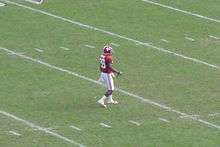 American football player waiting to field a punt on a green field.